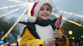 Cute preteen boy in Santa Claus hat is visiting outdoors festive in town square. A happy child is celebrating Christmas Eve on street Xmas fair. Wonderful and fairy tales winter holidays traditions. - Powered by Shutterstock - Get 15% off with code: PIKWIZARD15