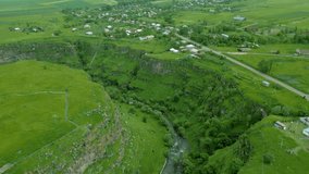 Aerial view of the grand canyon with steep rocky walls, overgrown with green grass and trees, in summer in cloudy weather. Along the banks are villages, fields. Dzoraget Canyon, Lori fortress. Armenia