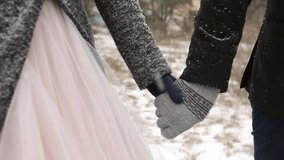 Close up video of groom leading bride by the hand walking at winter snow weather pine forest during snowfall. Snowing engagement ceremony.