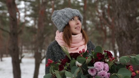 Portrait of beautiful mixed race caucasial asian girl holding a bouquet of flowers in winter snowy pine forest during snowfall and waiting for groom and first meet. Valentines Day concept.