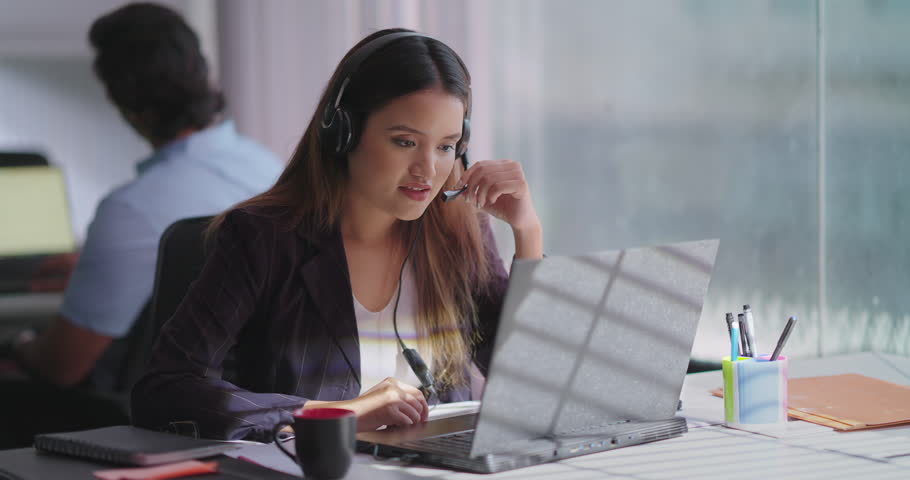 Indian happy woman wearing headphone sitting on chair using laptop talking online video call indoor office. Focused female agent provide customer support service communicate with client at workplace Royalty-Free Stock Footage #3391819107