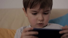 Little Boy Gamer Playing Video Game on Mobile Phone. Child Happy Playing Games With Phone. Preschooler Kid Plays Video Game On Smartphone. Harm for Mental Kid Health Eyesight Gambling Addiction.