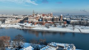 Krakow, Poland. Royal Wawel Cathedral and castle in snow in winter. Vistula river and tourist boats. Aerial approaching video with boulevard, promenades and walking people. Old city in the background