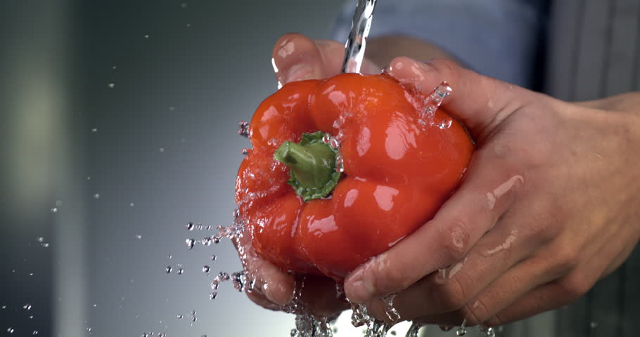 Super slow motion macro of splashing water drops are falling on fresh ripe organic single red sweet bell pepper while being washed by chef  in kitchen of restaurant before be cooked.