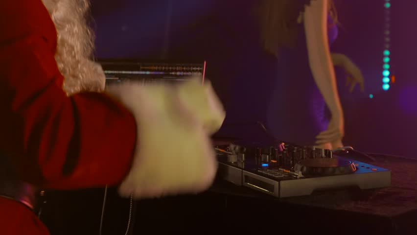 DJ Santa Claus mixing tracks in a nightclub at a Christmas and New Year party or Corporate events. Senior disc jockey as Santa listening music, headphones, laptop, mixer controller player, turntable. | Shutterstock HD Video #3392122603