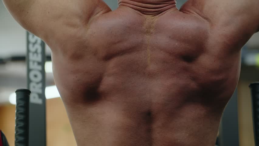 Young man bodybuilder is doing pull up in the gym on the horizontal bar. Training the muscles of the arms, back and neck. Showcasing the beauty and power of body, strength and endurance.