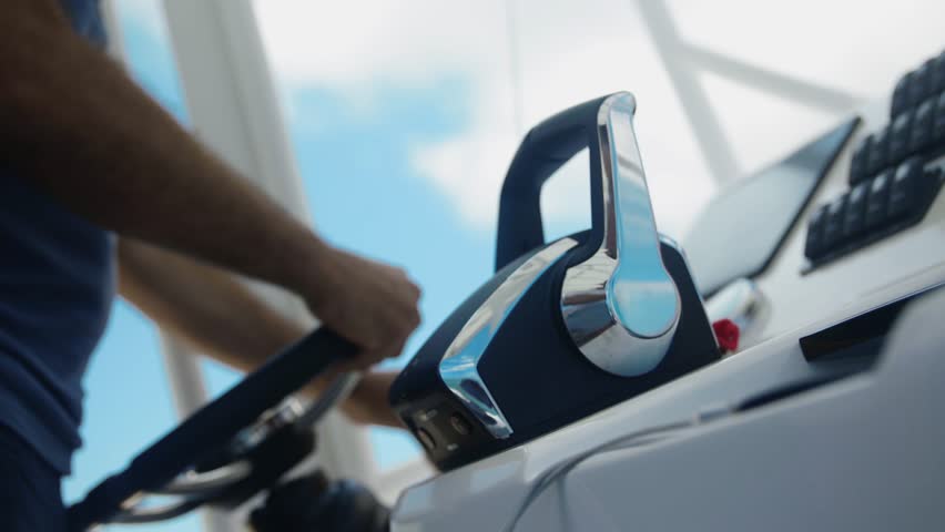 A man navigates a luxury boat, hands on the helm and speed control lever, the wind gently blowing. The frame captures the opulent cockpit(console) of the boat. Royalty-Free Stock Footage #3392207563