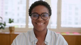 Front view on African-American businesswoman using laptop sitting at the desk at office, smiling charismatic female employee, freelancer wearing casual blue shirt and glasses working - Powered by Shutterstock - Get 15% off with code: PIKWIZARD15