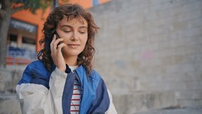 Cool hipster calling mobile phone relaxing at city weekend alone zoom out. Curly carefree girl talking cellphone sitting at brick wall. Trendy calm female teenager making order by smartphone outdoors. - Powered by Shutterstock - Get 15% off with code: PIKWIZARD15
