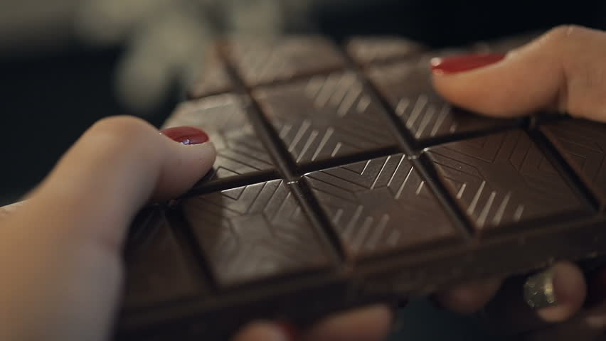 Woman breaks chocolate bar. Hands breaking, cracking dark milk chocolate. Person chef chocolatier snapping apart pieces of sweet chocolate for melting and making sweets desserts. Slow motion Royalty-Free Stock Footage #33923815