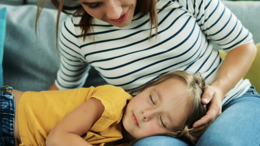 Good looking mother whispering in the ear of her cute little daughter who lying with her head on mom