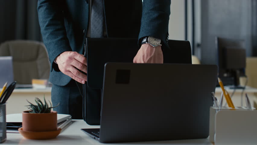 Cropped shot of unrecognisable businessman packing laptop and paperwork into briefcase and leaving office Royalty-Free Stock Footage #3392543443