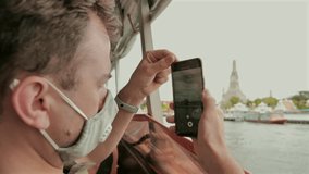Man wearing mask captures scenic views on boat ride. Travel during pandemic.