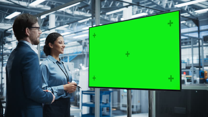 Meeting In Office Of Autonomous Factory With Robotic Arms: Hispanic Female Chief Engineer Talking with Caucasian Male Business Partner in a Conference Room with TV with Green Screen Mock Up Display. Royalty-Free Stock Footage #3392592253