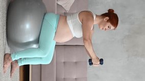 Pregnant woman doing exercises with dumbbells while sitting on a fitness ball at home. Vertical video.  - Powered by Shutterstock - Get 15% off with code: PIKWIZARD15