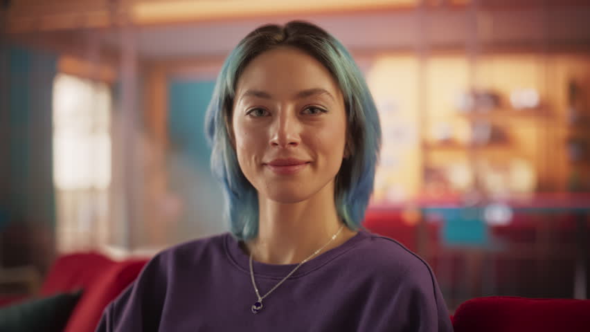 Slow Motion Portrait of Beautiful Stylish Woman with Blue Hair Looking Up to the Camera and Smiling Charmingly. Successful Young Woman Resting in Bright Living Room in Colorful Apartment
