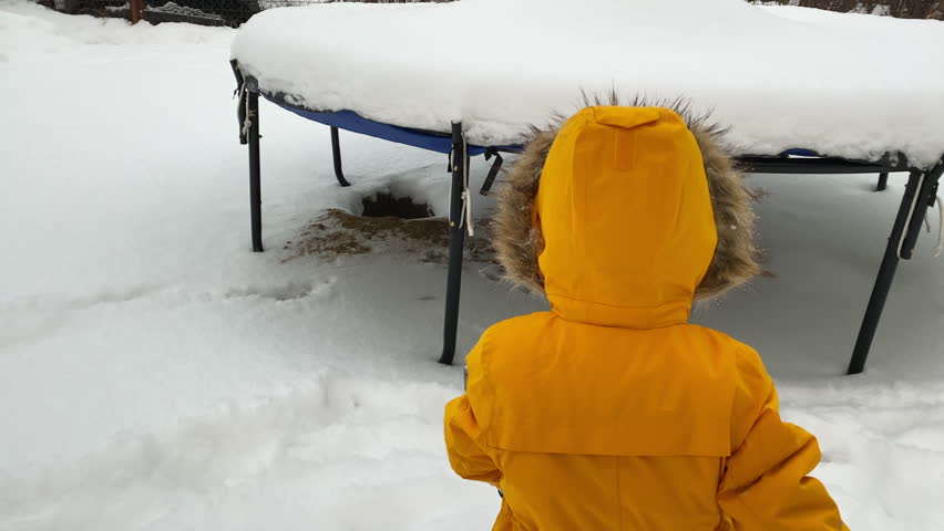 happy child playing in snowy yard in winter little boy removing snow from trampoline