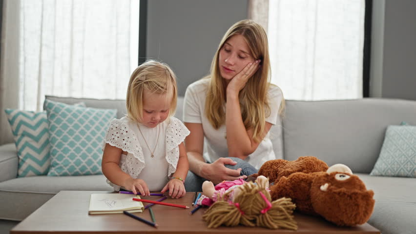 Stressed mother relaxing on sofa at home while little caucasian daughter seriously engages in drawing on notebook indoors Royalty-Free Stock Footage #3392755781