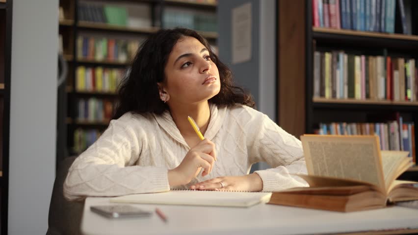 Portrait of doubtful young pretty woman student thinks questioningly searching inspiration and find solution idea answer with raised finger writing notes sitting at desk in university library  Royalty-Free Stock Footage #3392757727