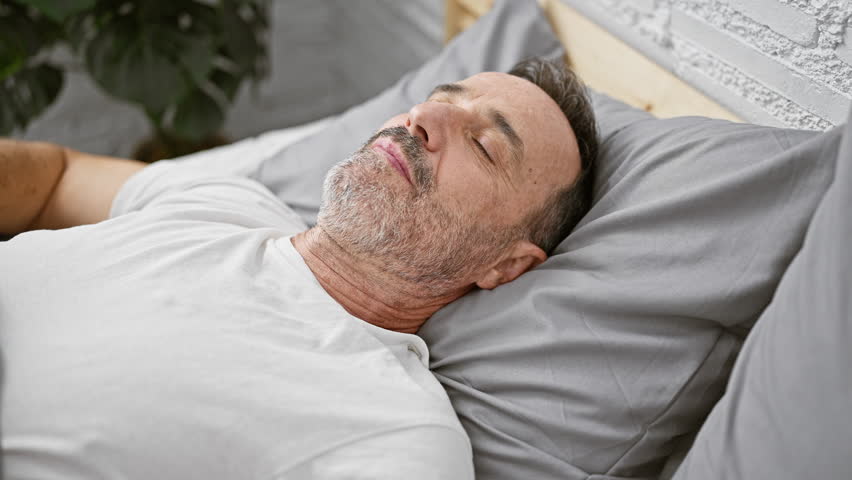 Middle-aged man with grey hair, seriously ill with covid-19, persistently coughing, lying in his comfy bedroom bed under a warming blanket, fighting the flu in his apartment's interior Royalty-Free Stock Footage #3392767169