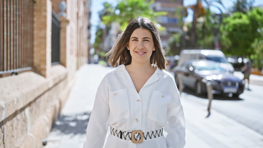 Young beautiful hispanic woman standing smiling at the street