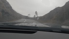 First person view, FPV, from dashcam of car driving along the Alentejo Coast in Portugal towards Sagres during a storm. Road trip video in POV, with rain and dark skies