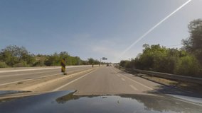 First person view, FPV, from dashcam of car driving along the Algarve Coast in Portugal outside of Portimao towards the Benagil Caves, driving on the highway. Road trip video in POV, with blue sky