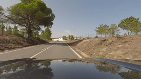 First person view, FPV, from dashcam of car driving along the Alentejo Coast in Portugal, passing cork oak trees and sand dunes. Road trip video in POV, with blue and clear sky on an empty road
