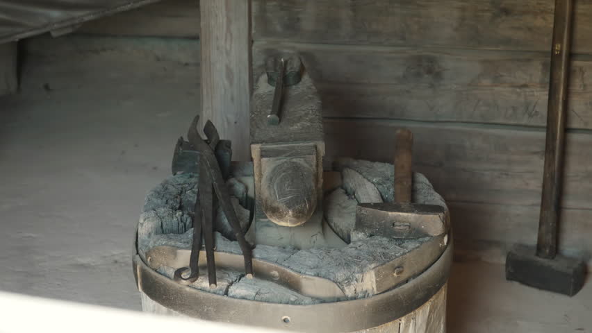 Old abandoned anvil with tongs and hammer in forge. Blacksmith tools for demonstration to tourists. Devices for forging hot metal in daylight.