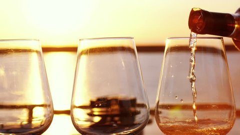 Pouring white wine in glass in slow motion at amazing sunset with sea view in a beach restaurant. 3840x2160