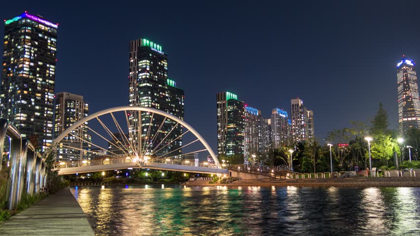 Time lapse of Skyscraper building with bridge illumination on songdo river in central park at Incheon, South Korea