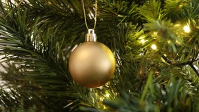 Matte gold color Christmas ornament 4K 2160p 30fps UltraHD footage - Bauble with fairy-lights on the artificial tree branch close-up 3840X2160 UHD video