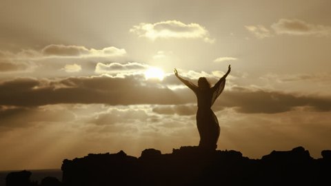 Handheld slow motion shot of woman meditating on a clifftop at sunset in 25P. 30P versions also available.