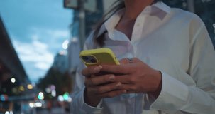 Focus on entrepreneur texting smart phone standing over night city street full of neon light. Female texting smart phone entrepreneur texting smart phone posting social media, scrolling news side view