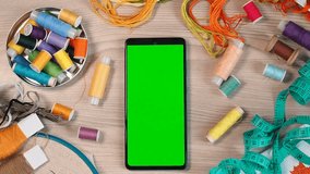 Smartphone with a green screen, chroma key mockup for the application. Concept of needlework, sewing or embroidery with threads. Background with colored threads.