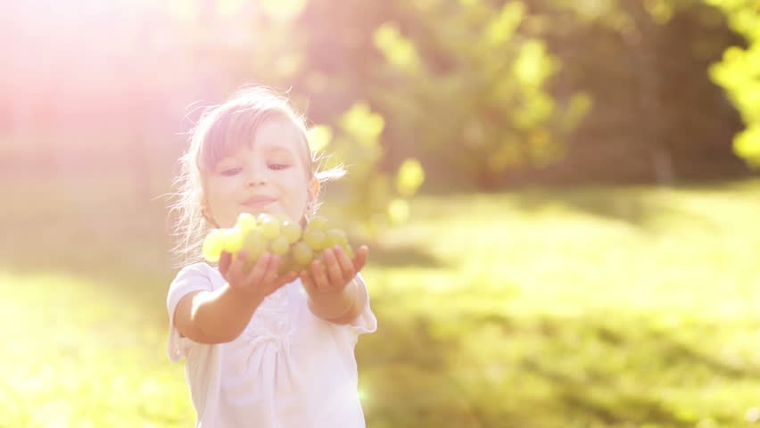 Girl treats the viewer grapes. Slow motion. Lens flare
