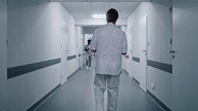 Doctor in white uniform walks medical center corridor, greets with African American colleague and talks with female physician. Multi ethnic medical staff in hospital hallway. Tracking shot. Back view. - Powered by Shutterstock - Get 15% off with code: PIKWIZARD15