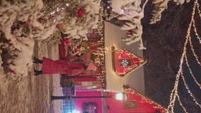 Vertical shot of beautiful woman in red coat walking near Santa Claus house and Christmas tree lights decoration while snowing at night. Fairytale winter wonderland season scene - Powered by Shutterstock - Get 15% off with code: PIKWIZARD15