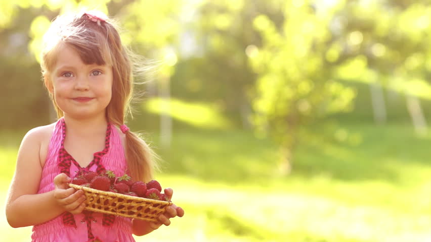 Girl holding basket of strawberries outdoors in sunny day. Slow motion
