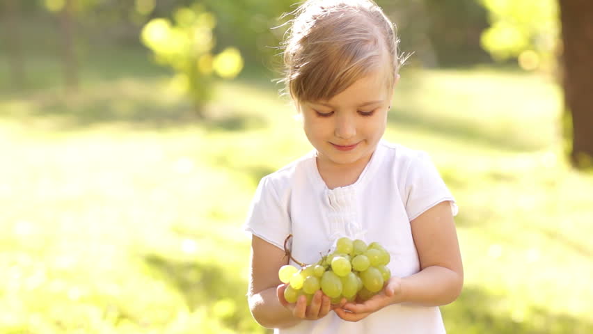 Smiling happy little girl with grapes in sunny day. Slow motion
