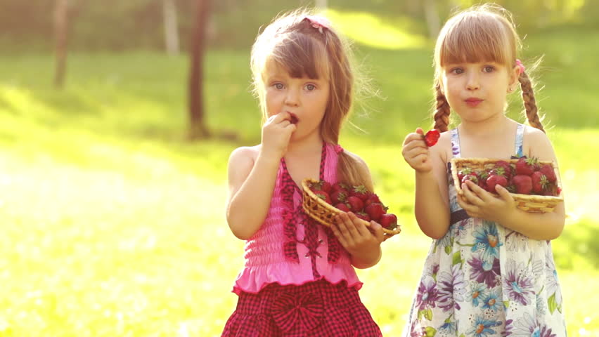 Two girls eating strawberries in sunny day. Slow motion
