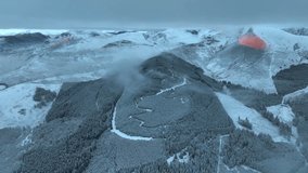 Sunrise casting orange relief of mountain shadow on snowy peak with frosty pine forest low cloud ceiling and distant snowy mountains. Whinlatter Forest, English Lake District, Cumbria, UK. - Powered by Shutterstock - Get 15% off with code: PIKWIZARD15