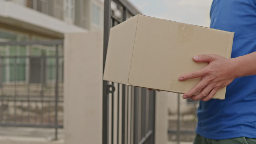 Delivery man driver in blue uniform is sending parcel box package to customer' hands from cargo truck at home