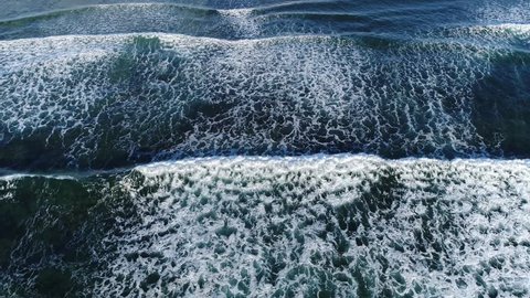 Aerial top down view of ocean waves breaking on reef showing beautiful and large ocean waves creating white foam and moving forward steady shallow water near mediterranean location 4k quality