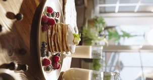 Pancakes with berries, syrup, and sugar powder in kitchen. Lifestyle, cooking, domestic life. Pleasant family traditions. Table decorated with berries, beautiful cinematic vertical promotional video