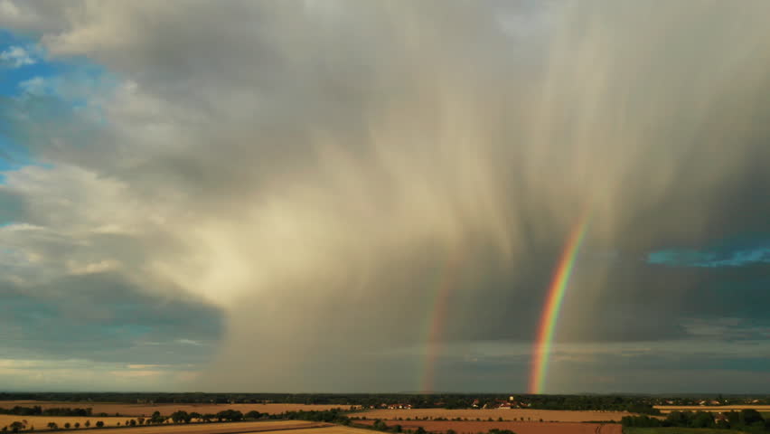 Double rainbow graces sky creating breathtaking scene. Field unfolds in soft glow of sunlight and colors of mesmerizing double rainbow