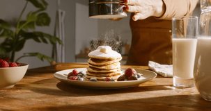 Unrecognizable person sprinkles powdered sugar on perfect stack of pancakes, aesthetically decorated with berries, in slow motion, in kitchen scene. Advertising cinematic. Healthy lifestyle, cooking
