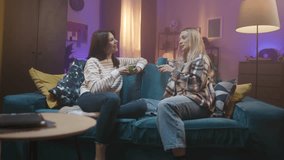 Two young girls are sitting on sofa face to face. Friends are having talk with cups of tea or coffee in hands. Girls communicate to each other and smiling. Cozy light room atmospere. - Powered by Shutterstock - Get 15% off with code: PIKWIZARD15