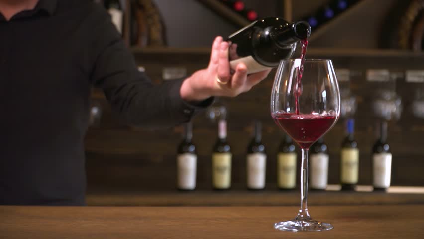 Red wine is beautifully poured into a glass. A bartender pours red wine into a glass. Production and sale of wine. 