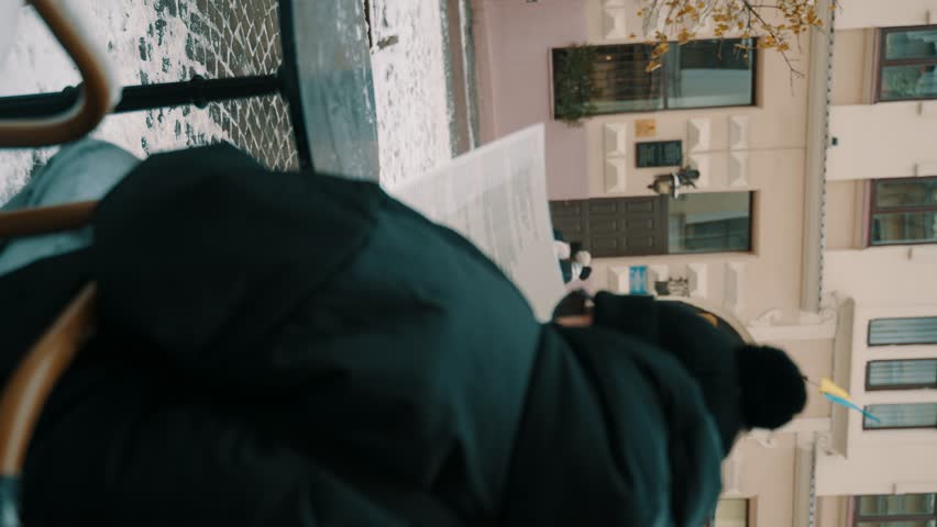 Two people in winter jackets and hats outdoors, one in the foreground is blurred and the other is walking in the background, looking straight ahead, i